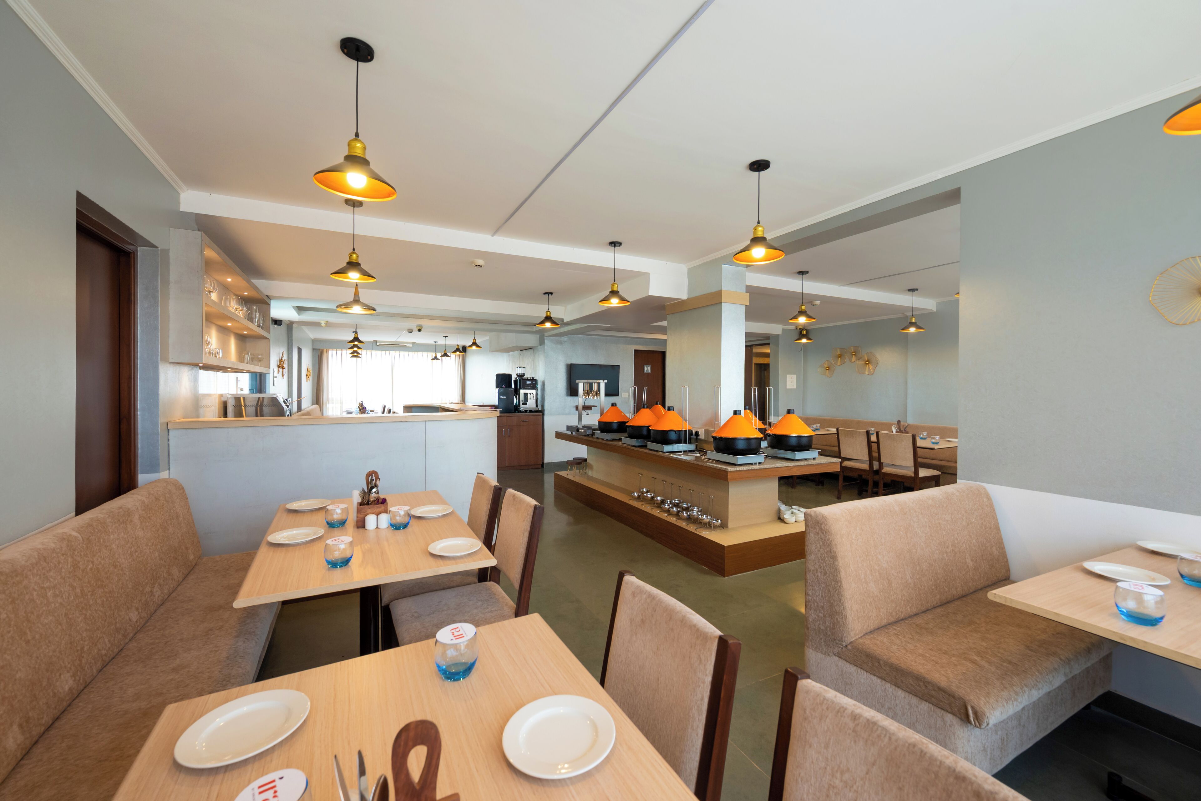 Un restaurante moderno con mesas y cabinas de madera, iluminación colgante y una zona central de servicio.