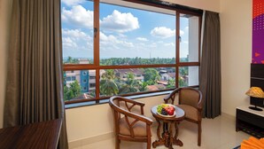 A room with a large window, two wooden chairs, a small round table with fruit, and a TV on a stand. - Ira by Orchid, Porvorim, Goa (Porvorim)