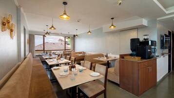 A dining area with multiple tables and benches, a kitchen area with appliances, and a view of the outdoors.