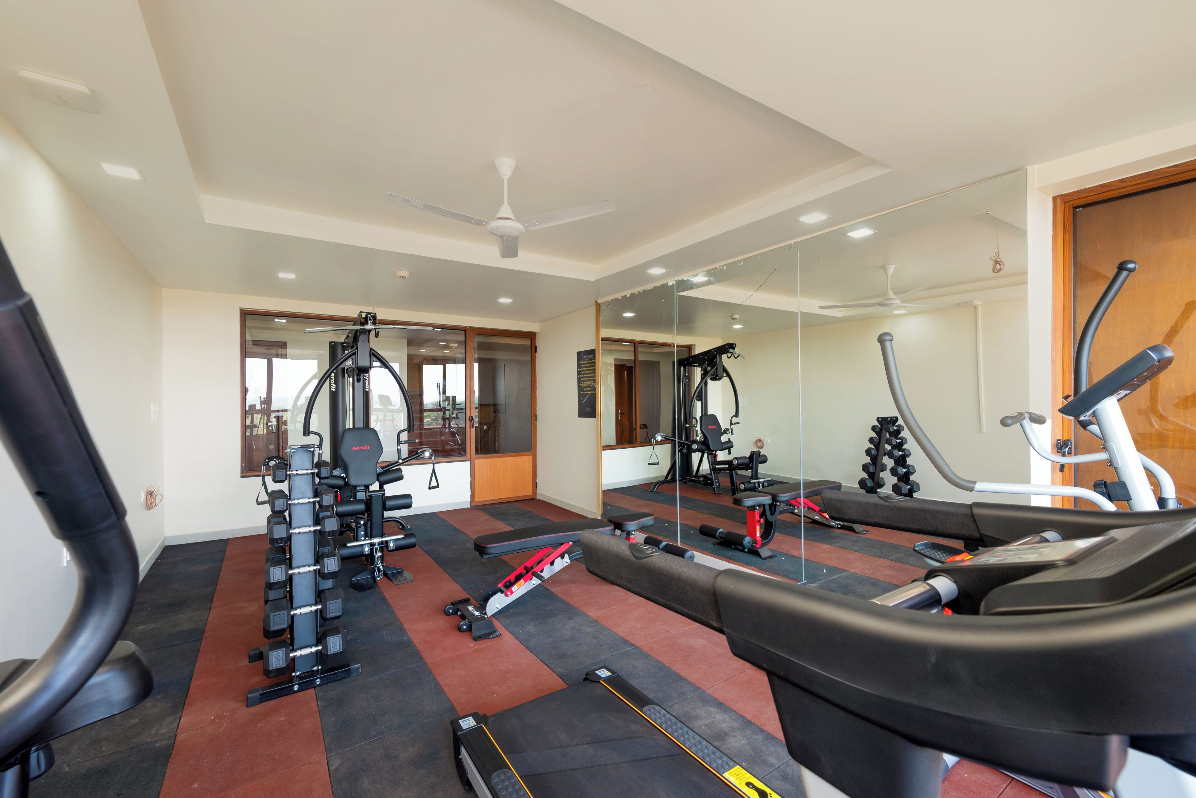 Een sportschool met fitnessapparatuur, een spiegel en een loopband.