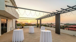 A rooftop terrace with round tables and candles, overlooking a cityscape at sunset. - Ira by Orchid, Porvorim, Goa (Porvorim)