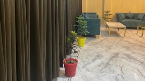 Vestíbulo de hotel con piso de mármol, un sofá verde, una planta en maceta amarilla y roja, y una pared cubierta de cortinas.