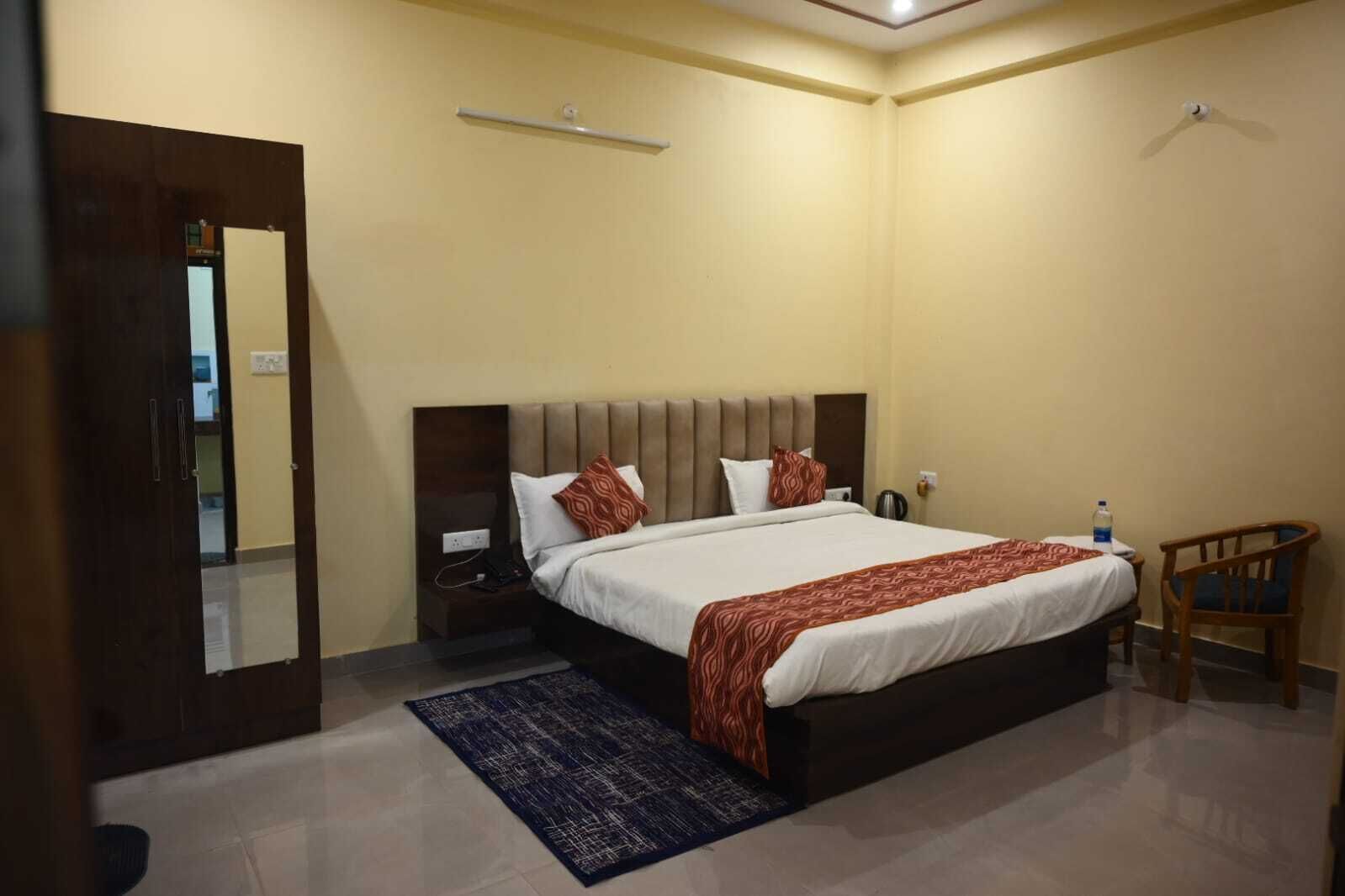 A neatly arranged bedroom with a bed, bedside tables, a chair, and a small table with a water bottle.