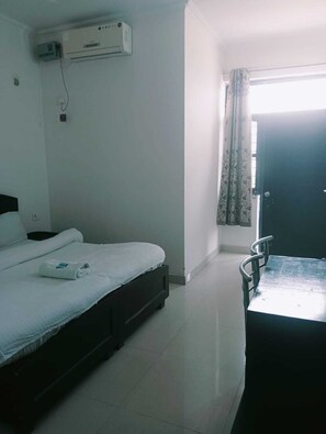 A hotel room with a bed, a desk, and a window with curtains. - Benison Guest House (Dehradun)