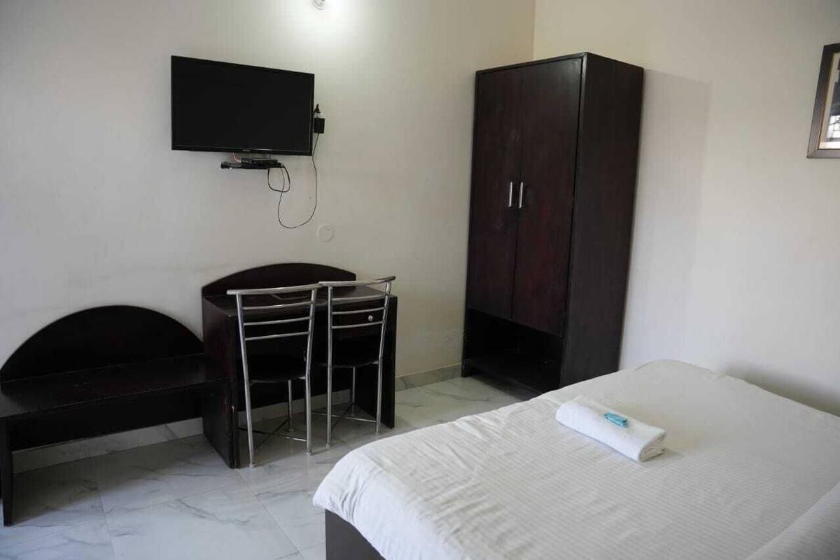Un dormitorio con cama, escritorio, silla, armario y televisor montado en la pared.