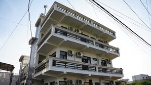 Un edificio de varios pisos con balcones, unidades de aire acondicionado y una entrada con reja.