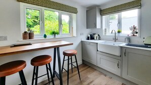 A modern kitchen with a wooden countertop, two stools, a sink, and a window with a view of greenery.