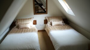 A bedroom with two single beds, a wooden headboard, a skylight, and a mirror on the wall.