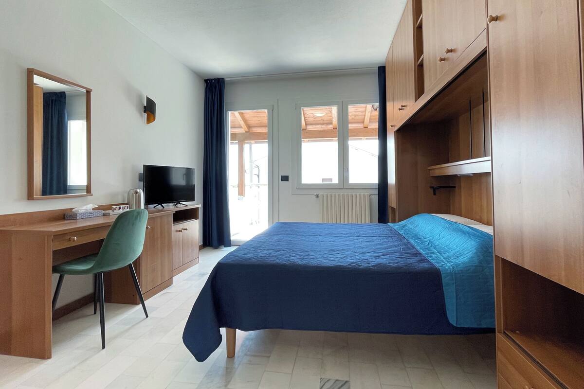 A bedroom with a bed, a desk, a chair, a television, and a wardrobe.