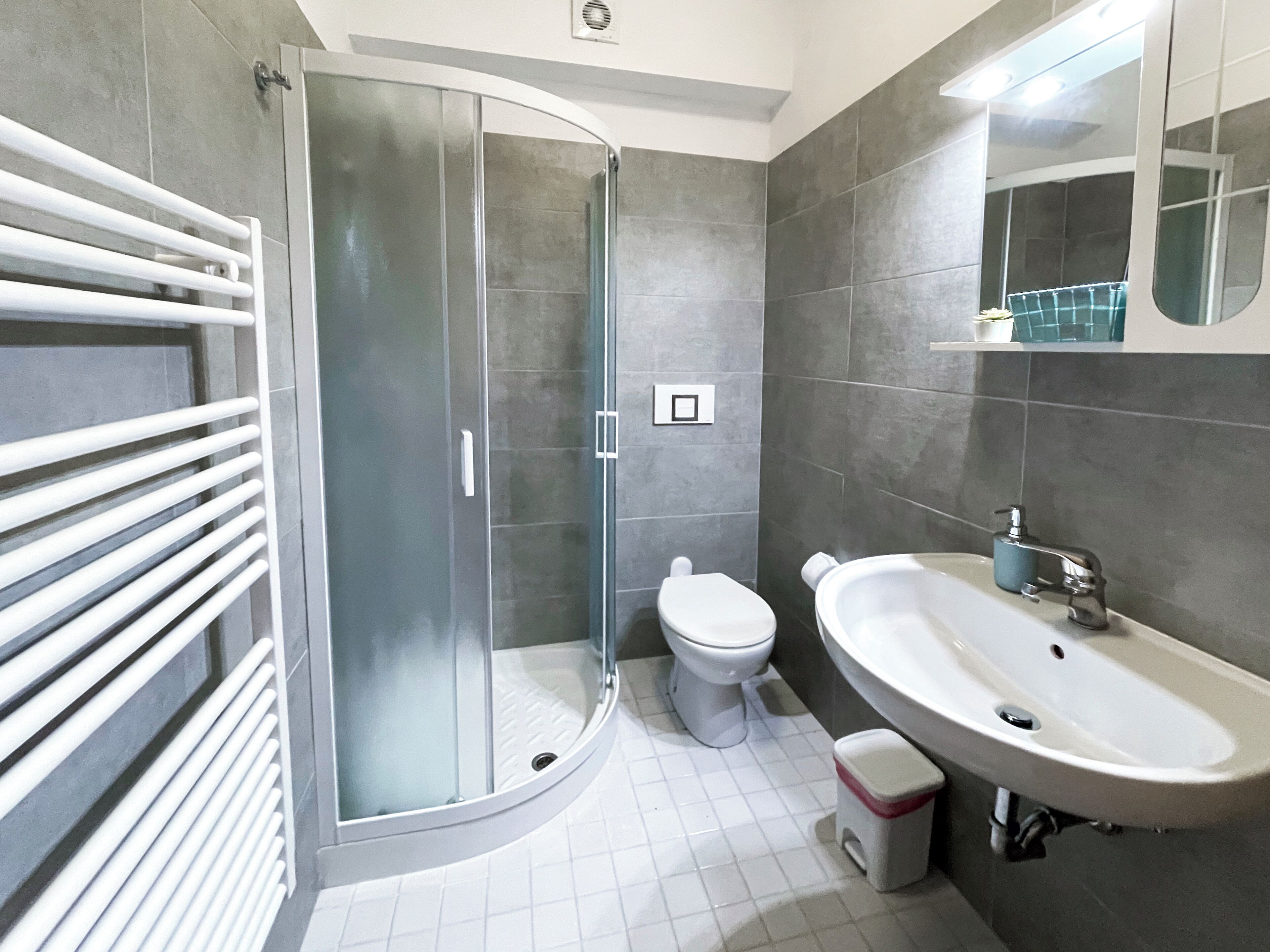 A modern bathroom with a glass shower enclosure, a toilet, a sink, and a small trash bin.