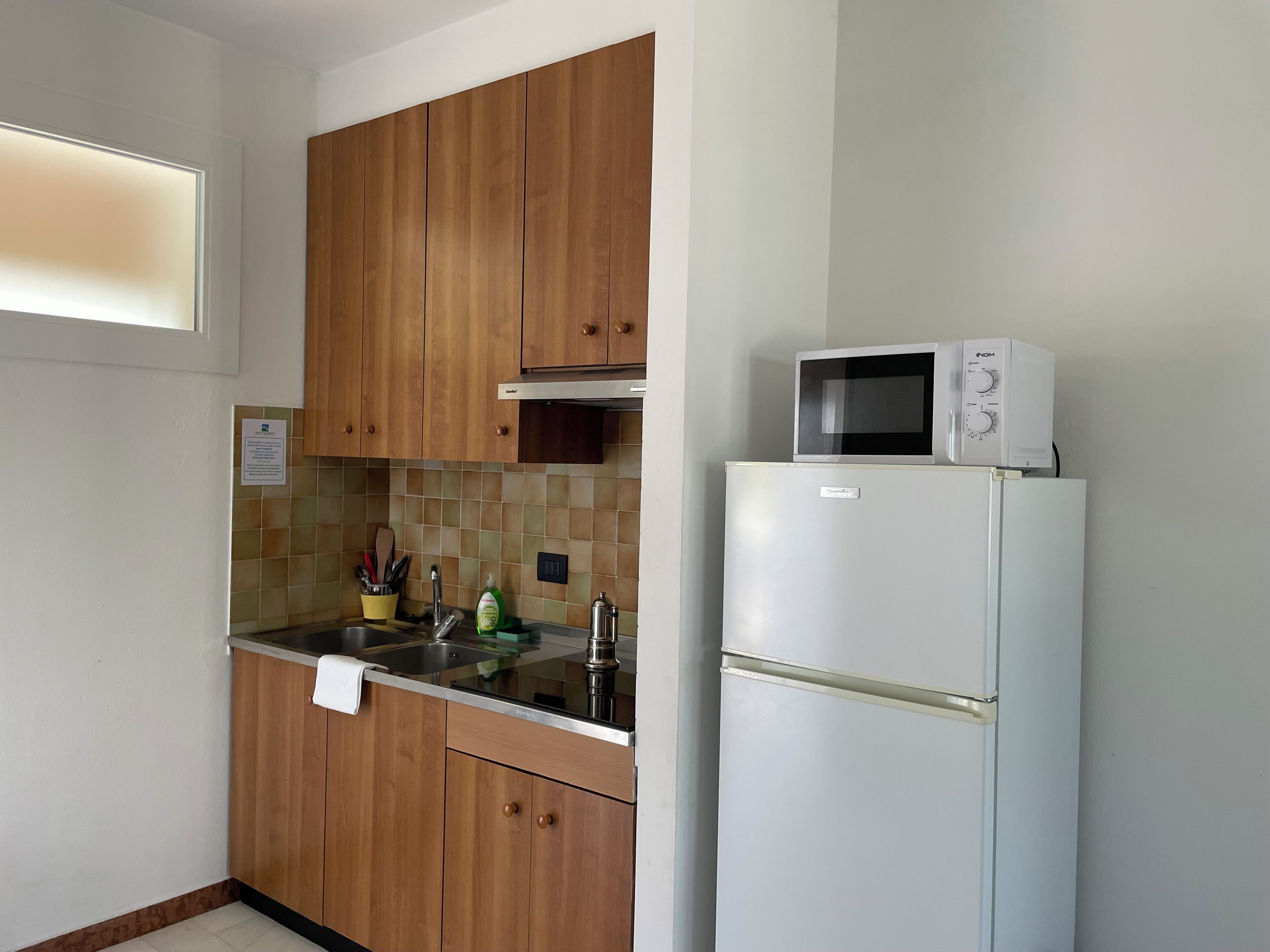 Una cocina con armarios de madera, un lavamanos de acero inoxidable, un microondas y un refrigerador.