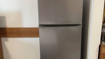 Un refrigerador gris con un microondas encima, situado en un rincón de una habitación con piso de madera y paredes blancas.