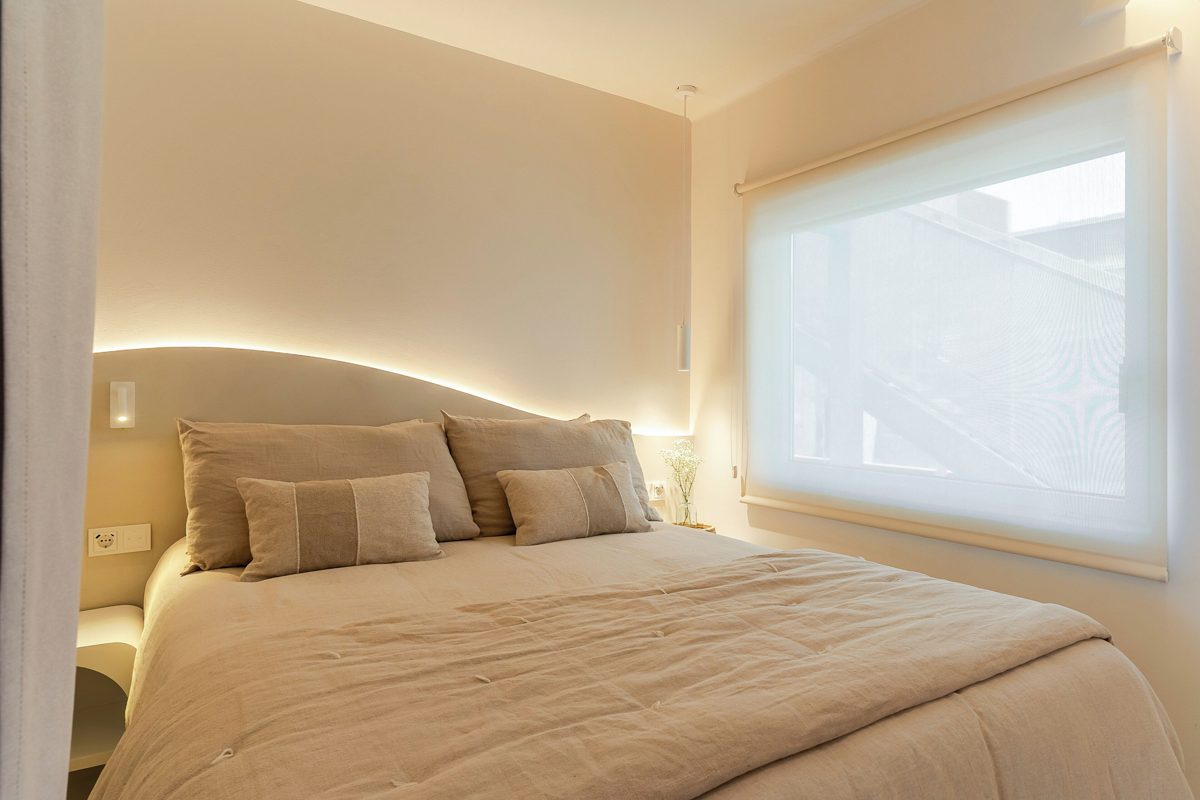 Une chambre avec un grand lit, une table de chevet et une fenêtre donnant sur des immeubles.