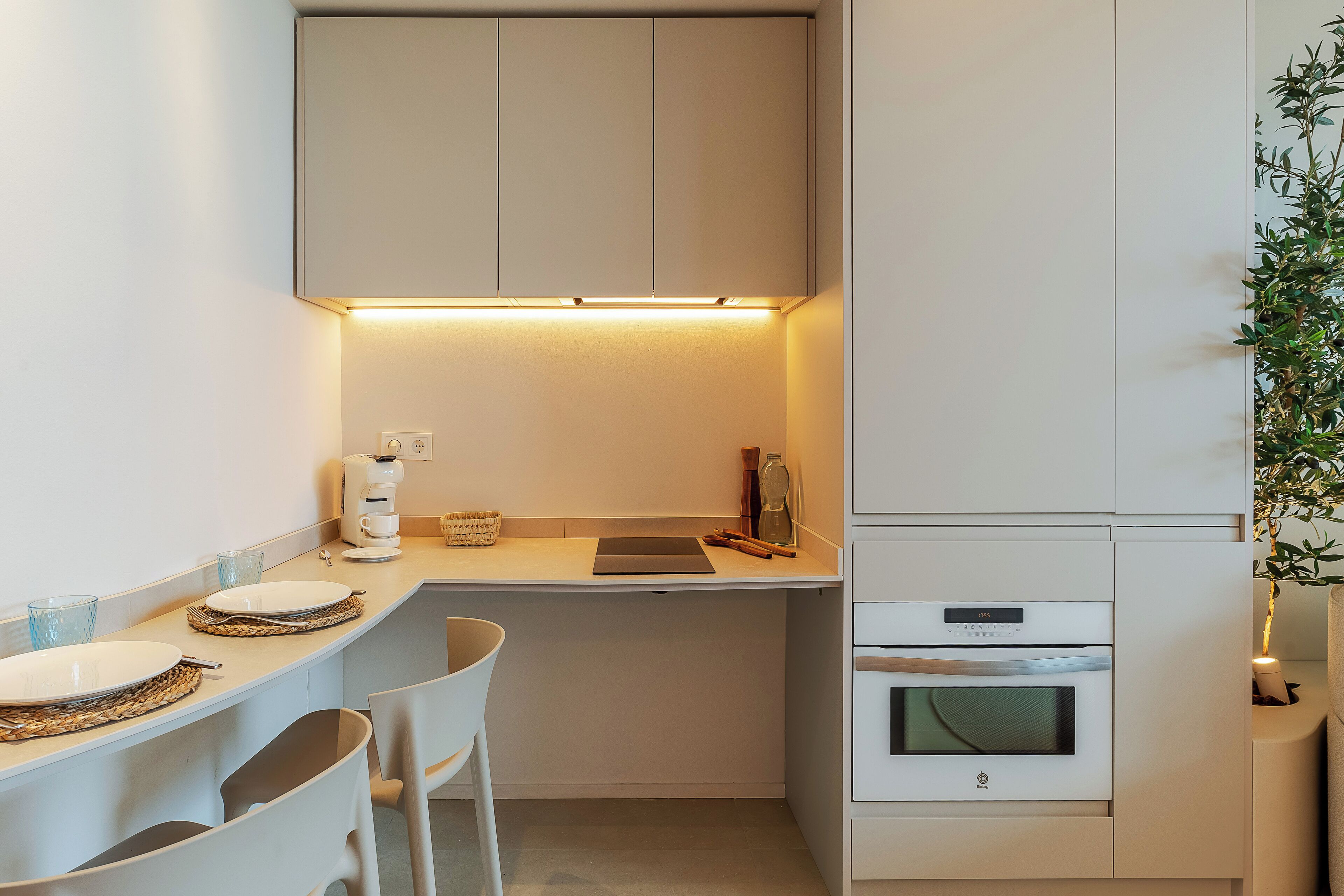 A compact kitchen with white cabinetry, a countertop, a coffee maker, a kettle, and a small oven.