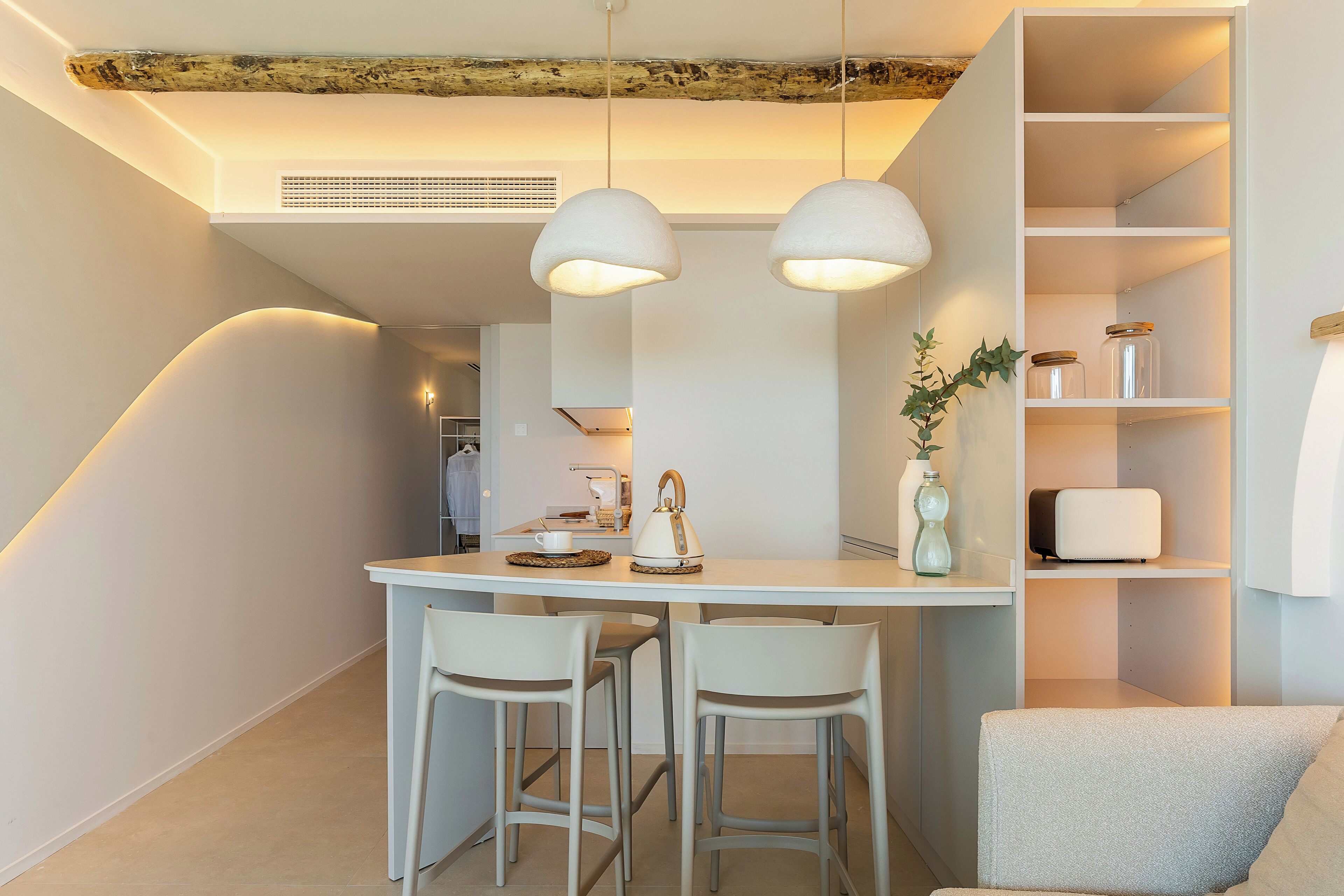 Ett modernt kök med en vit bänkskiva, två hänglampor och en inbyggd hylla med glasburkar.
