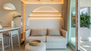 A modern living room with a sofa, a dining area with a table and chairs, and a large window with a view of greenery. - Apartamentos Azul (Castelldefels)