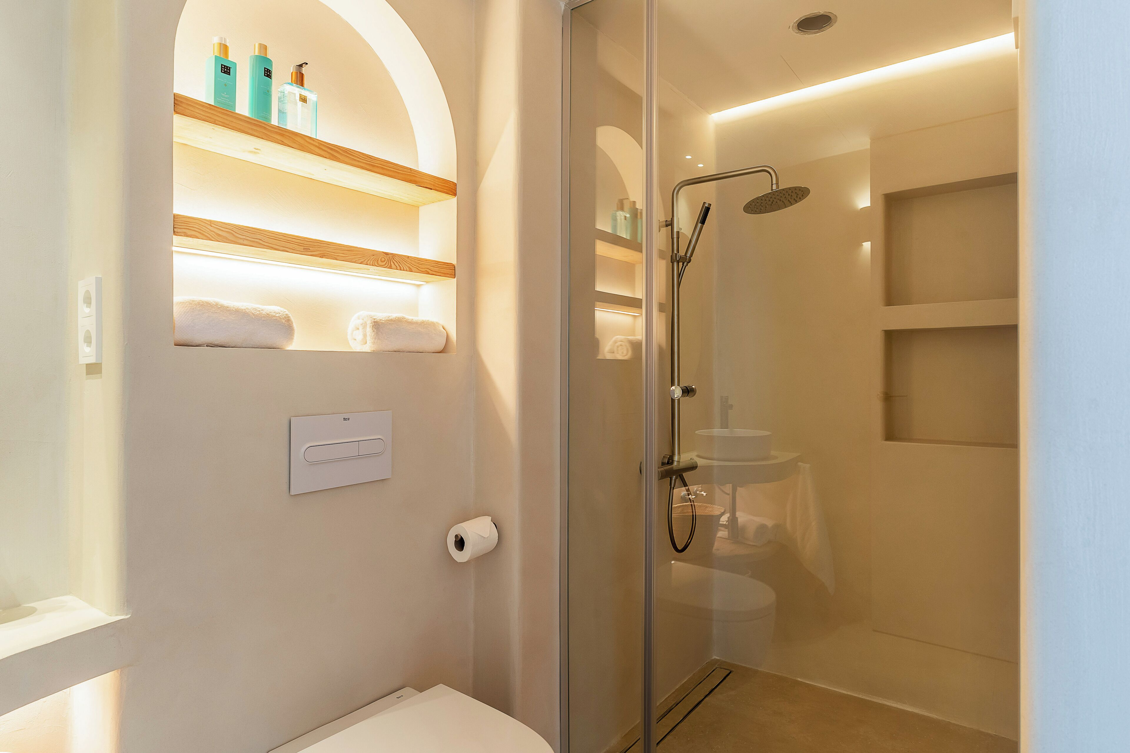 Un baño moderno con ducha acristalada, inodoro y repisa con artículos de aseo.