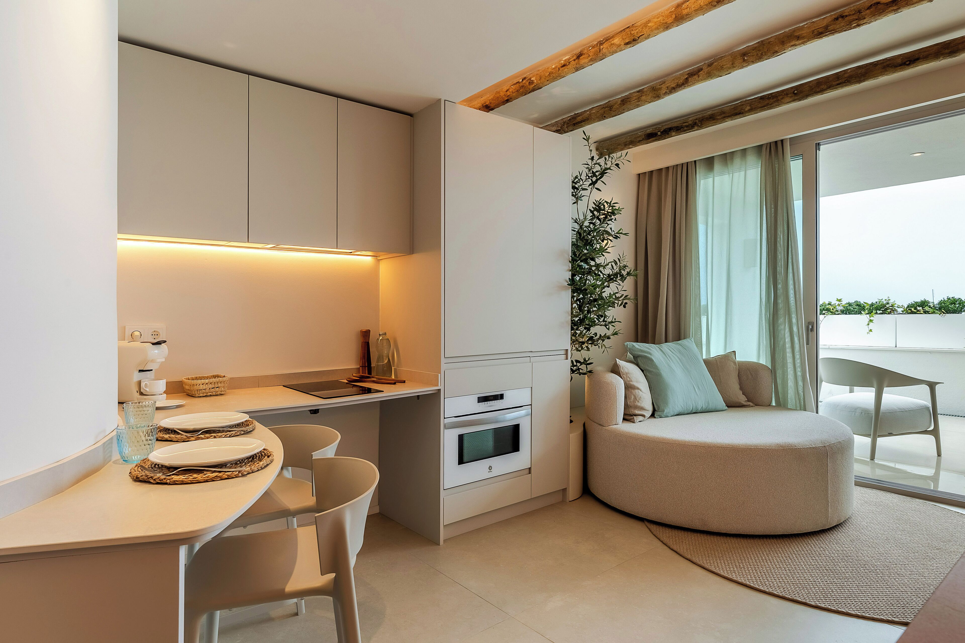 Una cocina moderna con electrodomésticos integrados, un comedor con sillas y una zona de estar acogedora con un pouf redondo.