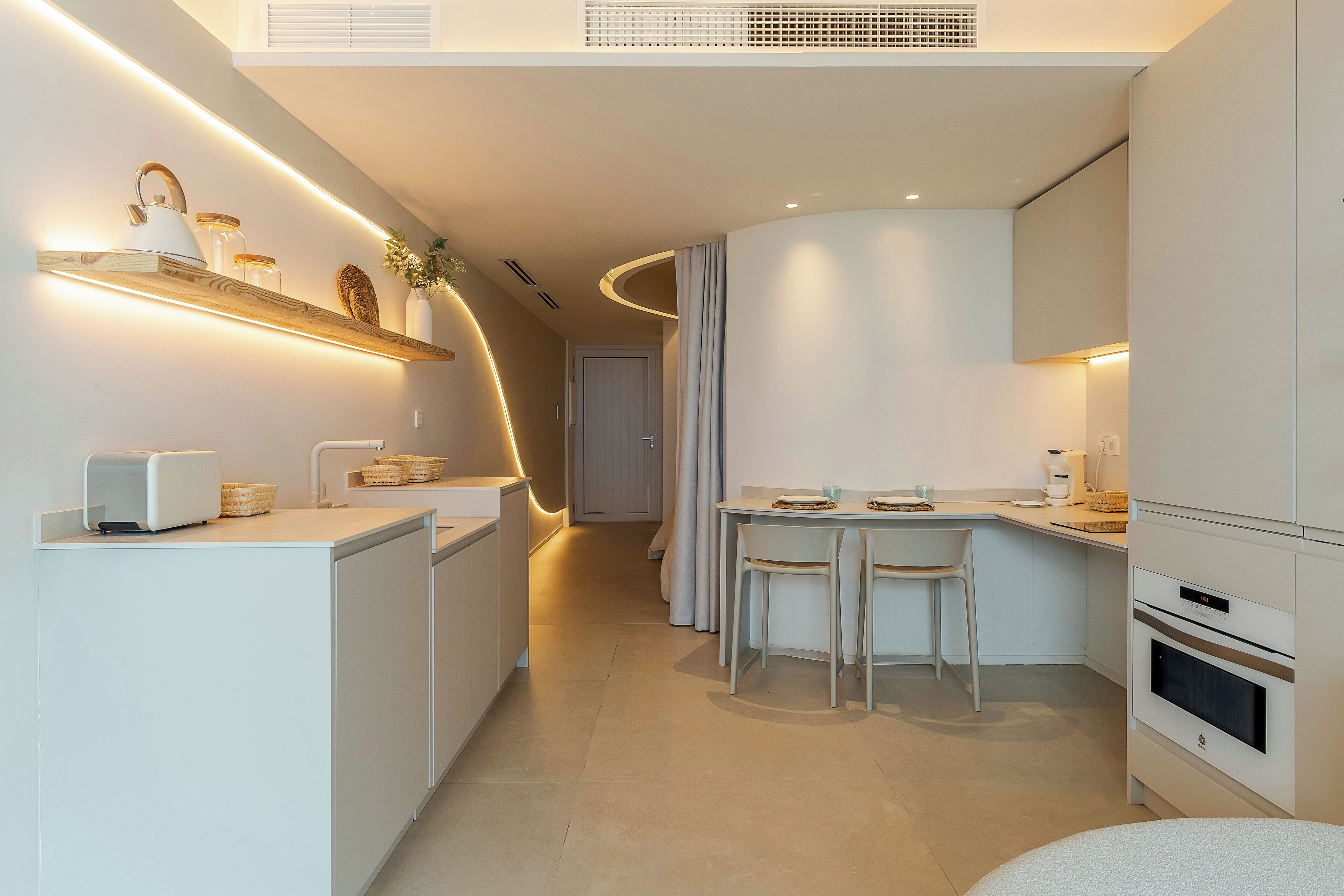Une cuisine moderne dotée d’appareils électroménagers intégrés, un coin repas avec une petite table et des chaises, et un plafond au design incurvé.