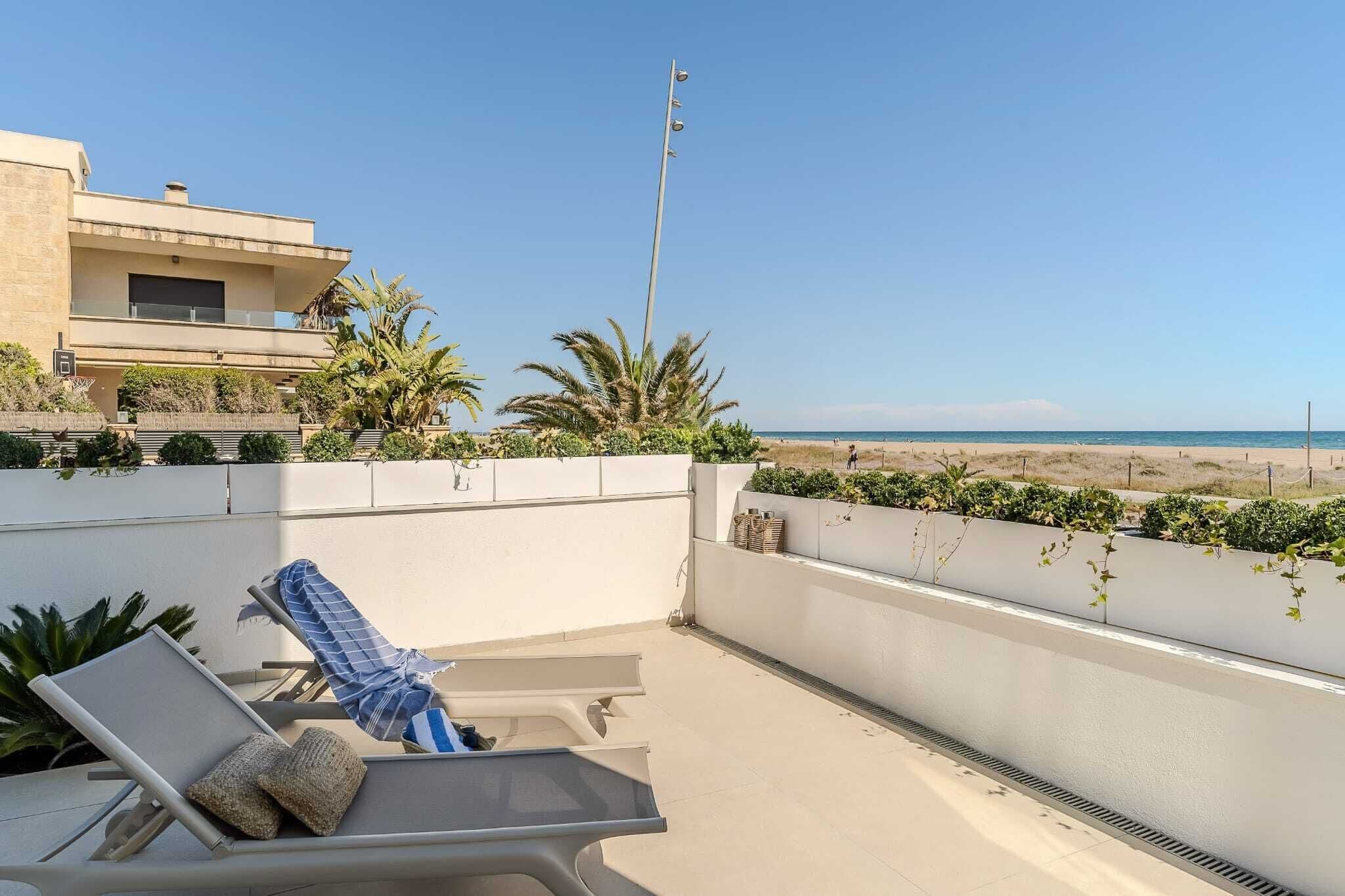 A rooftop terrace with a lounge chair and cushions, overlooking a beach and a clear sky.