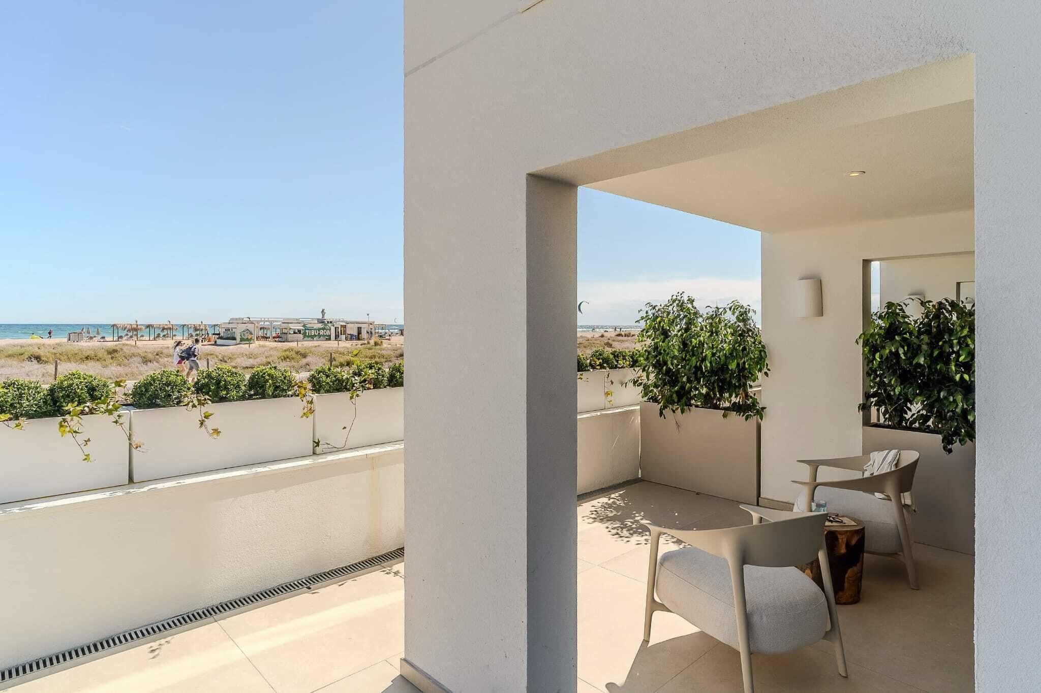 Un balcon avec vue sur la plage, une table, deux chaises et des plantes en pot.