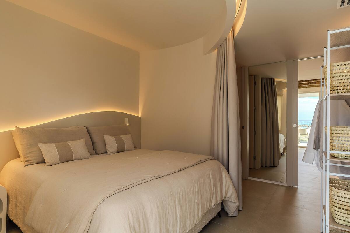 Un dormitorio con una cama grande, un armario con cestas y vistas a través de una puerta.