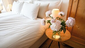 A neatly made bed with white linens, a vase with flowers on a wooden side table, and a lamp on the nightstand. - Residence Au Reduit - Living in the Heart of St. Moritz (San Maurizio)