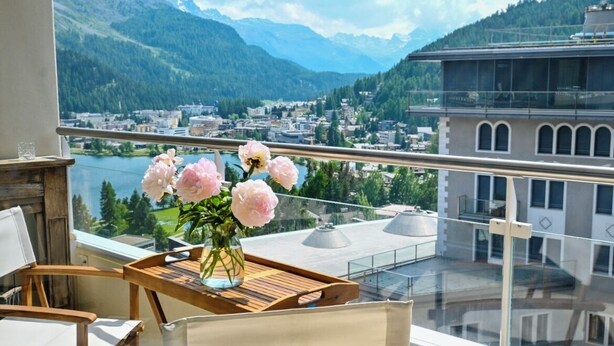 A balcony with a view of a mountainous town, a wooden table with a vase of flowers, and a chair. - Residence Au Reduit - Living in the Heart of St. Moritz (San Maurizio)