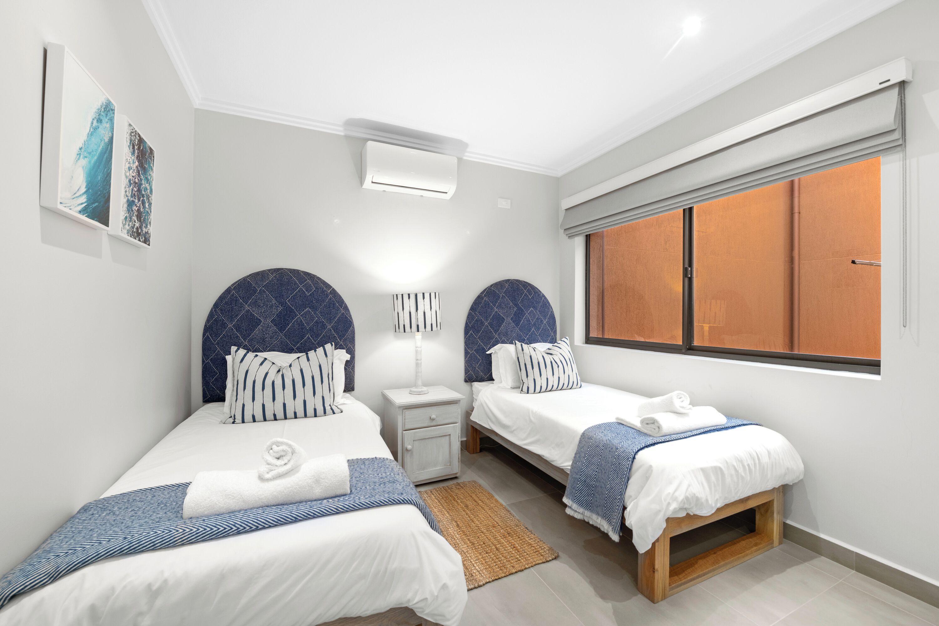 Une chambre d’hôtel moderne avec deux lits, une table de chevet, une lampe et une fenêtre avec des stores.