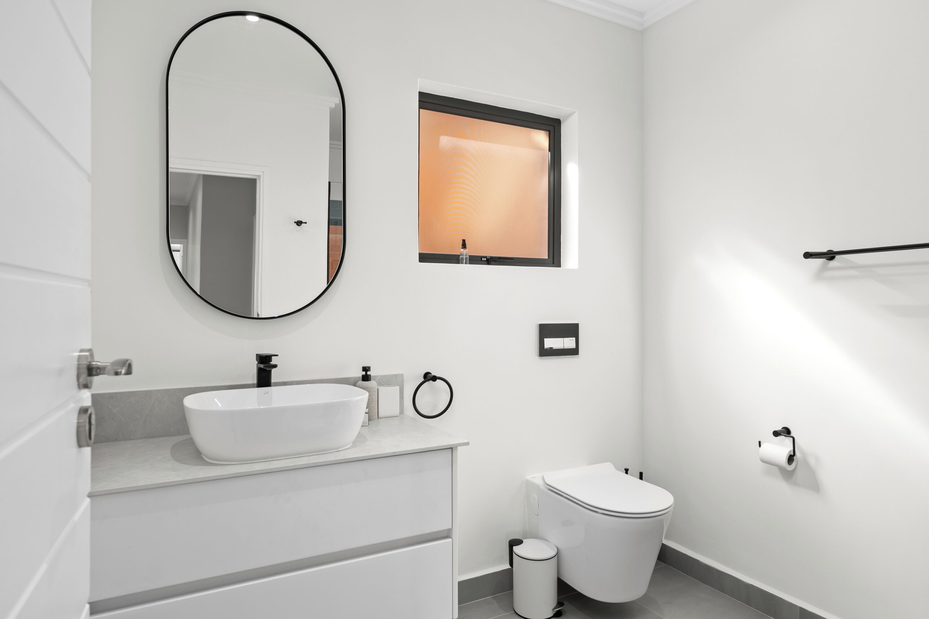 A modern bathroom with a white sink, mirror, and toilet.