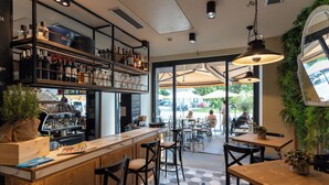 Un café con barra de madera, taburetes y mesas con sombrillas.