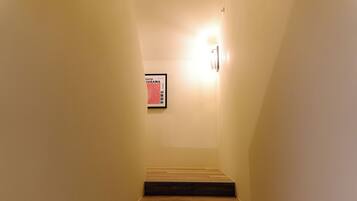 Eine schmale Treppe mit hölzernen Stufen, die nach oben führt, ein gerahmter Poster an der Wand und eine Wandleuchte.