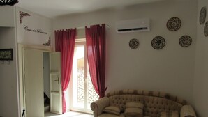 Un salón con un sofá color beige, cortinas rojas, un equipo de aire acondicionado y platos decorativos en la pared.