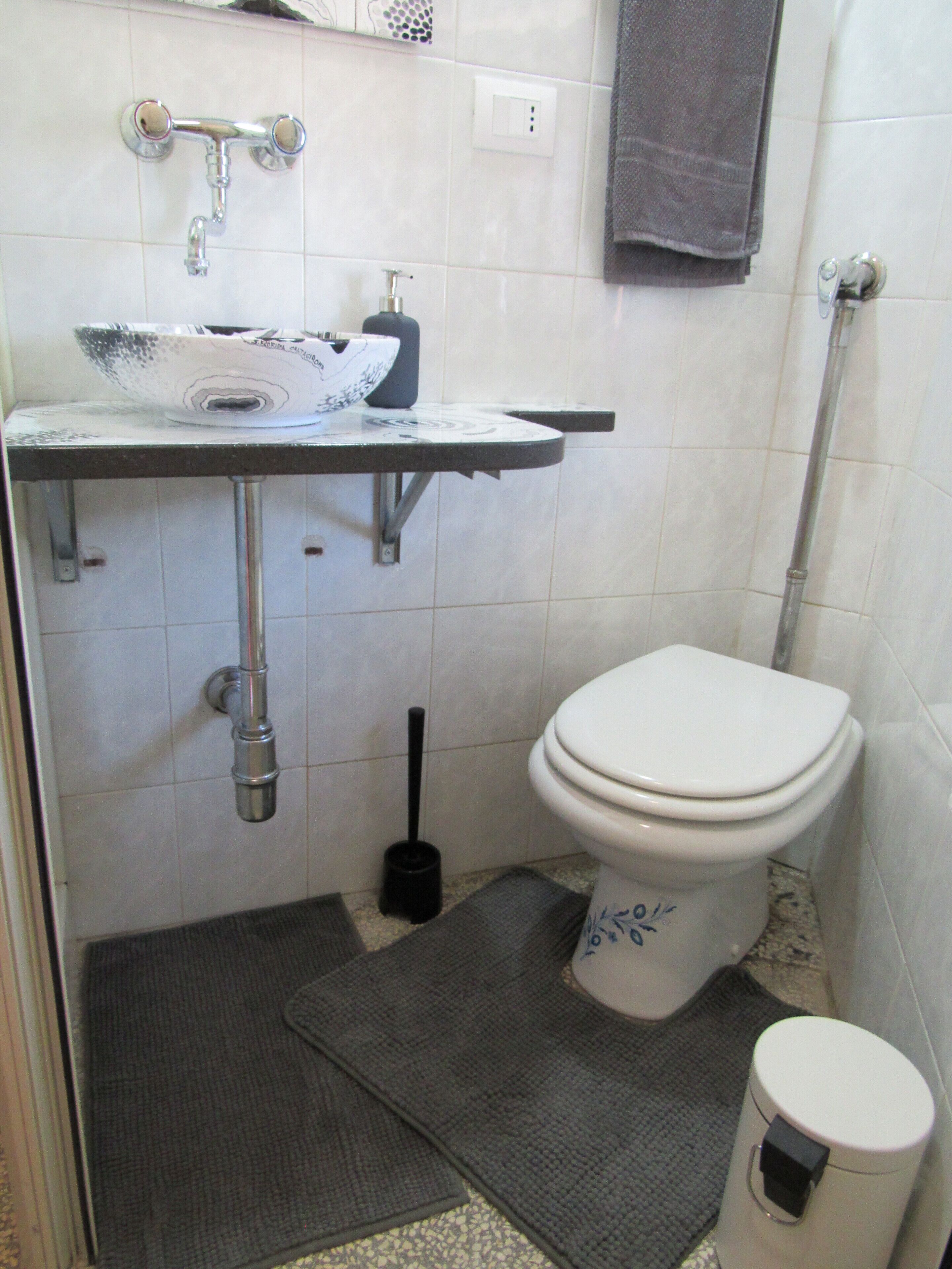 Ein kleines Badezimmer mit Toilette, Waschbecken mit Seifenspender und WC-Bürste.