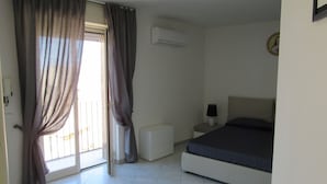 Un dormitorio con cama, mesita de noche, lámpara y ventana con cortinas.