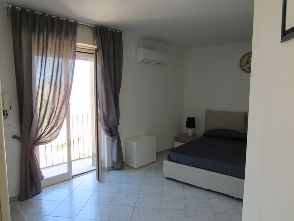 A bedroom with a bed, a nightstand, a lamp, and a window with curtains.