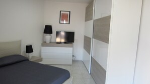 Un dormitorio con cama, televisión sobre una cómoda, lámpara y armario.