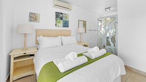 A neatly made bed with white linens and two rolled towels, a wooden nightstand with a lamp, and a green throw blanket. - San Lameer Villa 2532 (Southbroom)