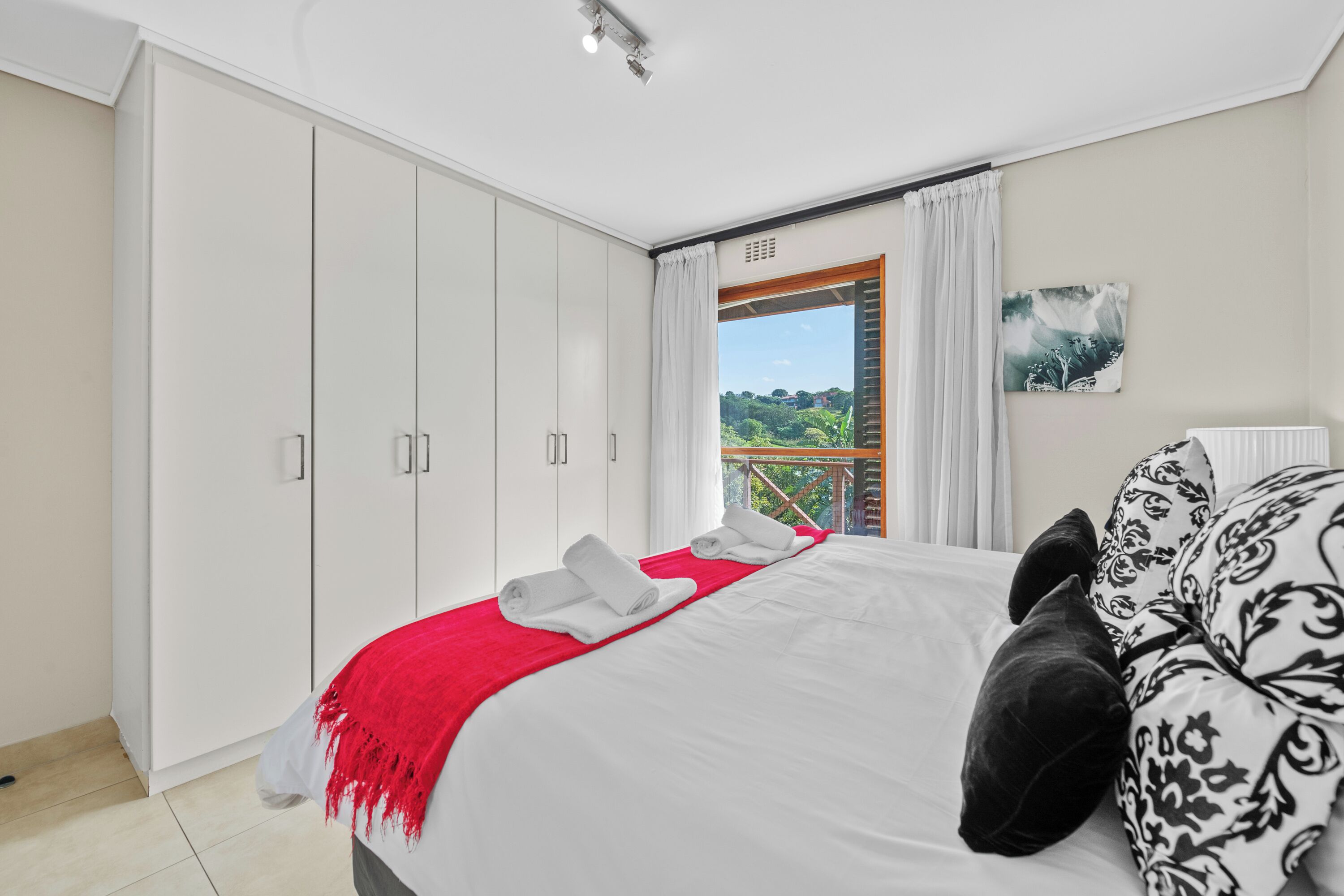A bedroom with a bed, white wardrobe, and a view of greenery through a window.