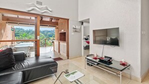 A modern living room with a black leather sofa, a glass coffee table, a flat-screen TV, and a balcony with a view of greenery. - San Lameer Villa 2532 (Southbroom)
