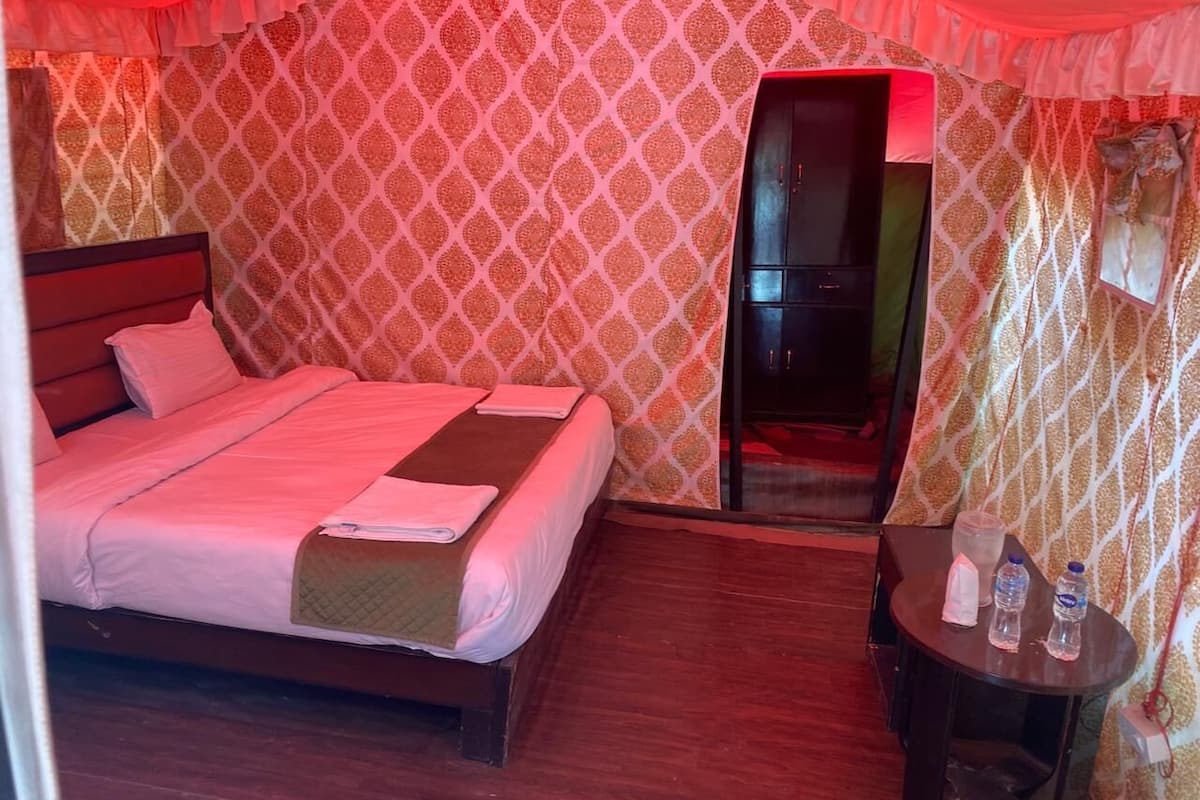 A hotel room with a bed, a small table with water bottles, and a door leading to another room.