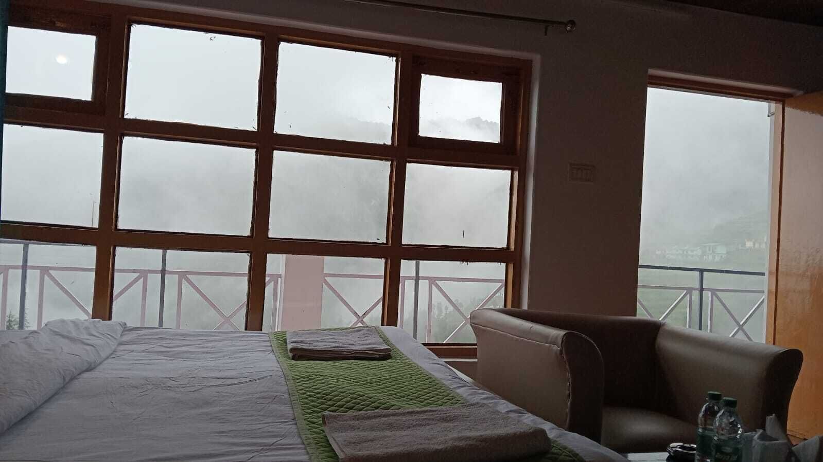 A hotel room with a bed, a chair, and large windows offering a view of a balcony.