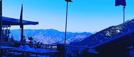 A snow-covered outdoor seating area with tables and chairs, flags, and a mountainous backdrop.