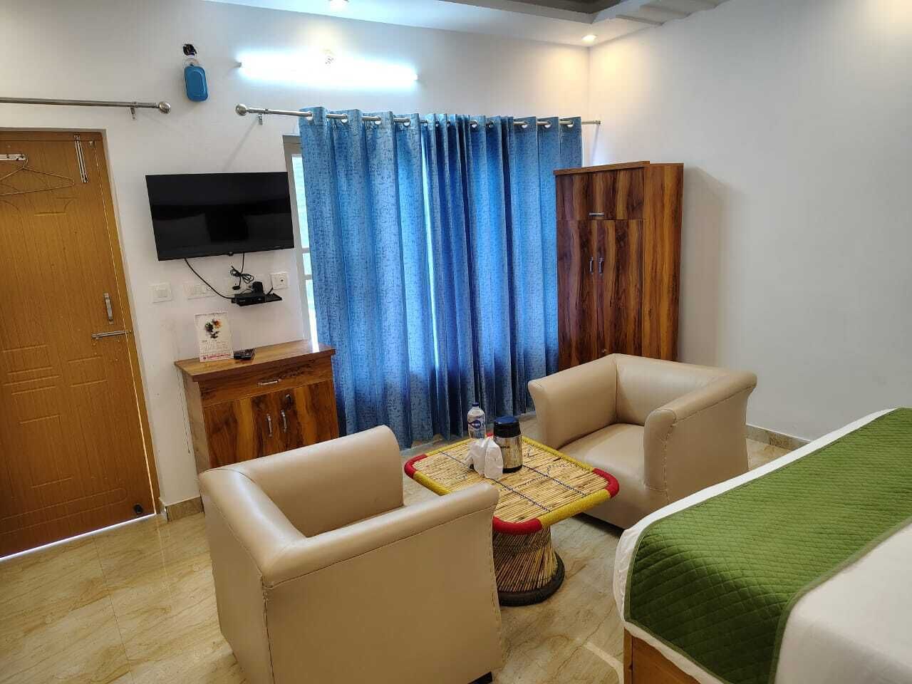 A hotel room with a bed, two chairs, a small table, a TV, a wardrobe, and a curtain.