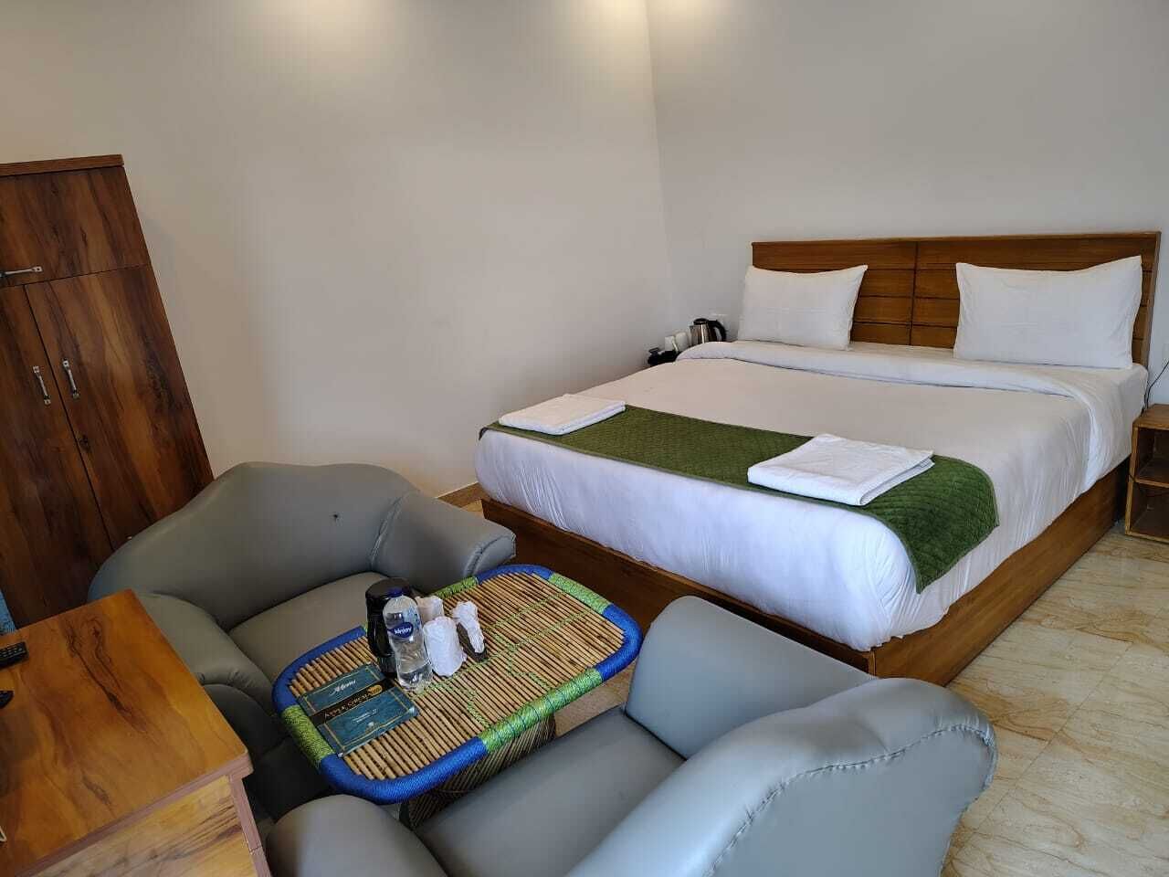 A hotel room with a bed, a sofa, a small table, and a wooden wardrobe.