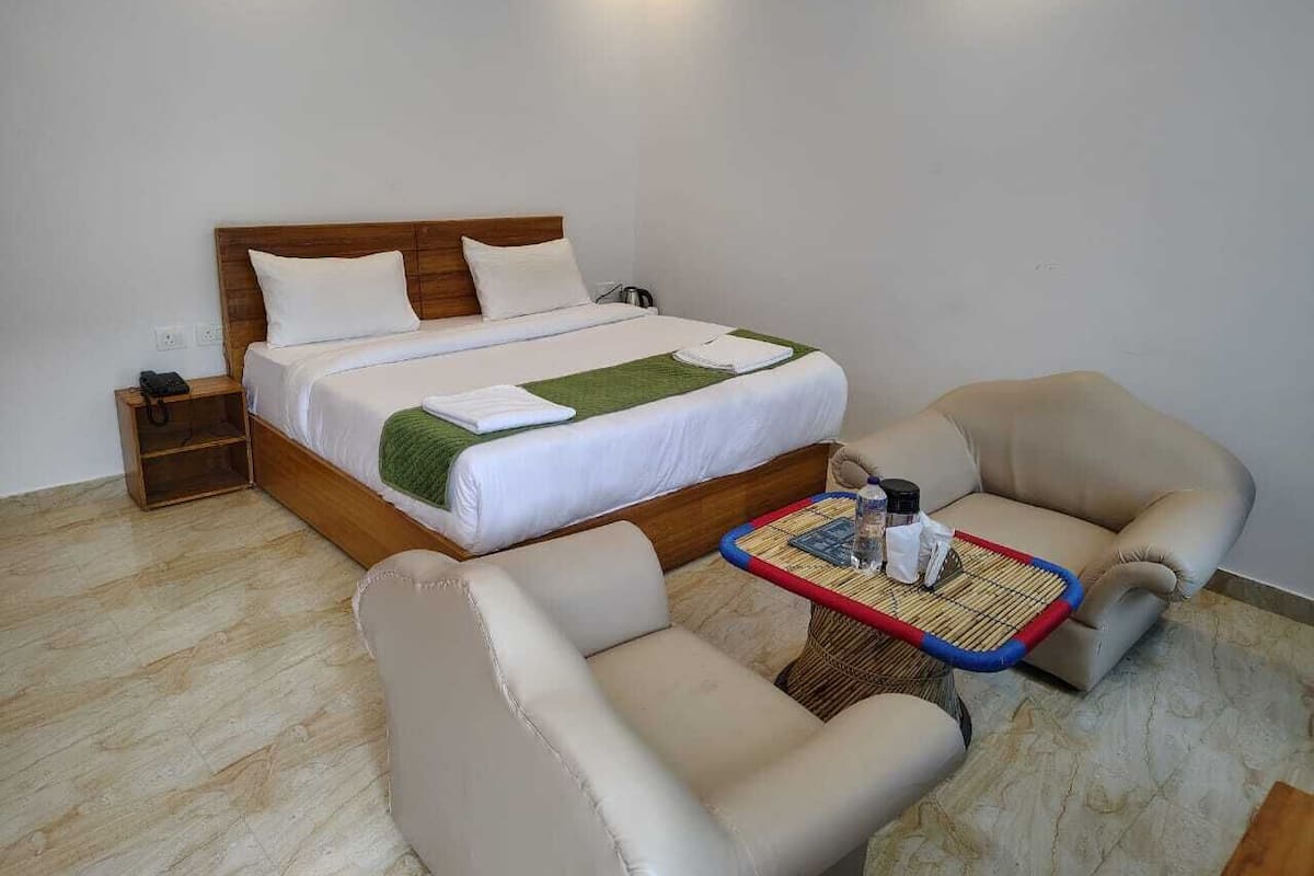 A hotel room with a bed, two armchairs, a small table, and a nightstand.
