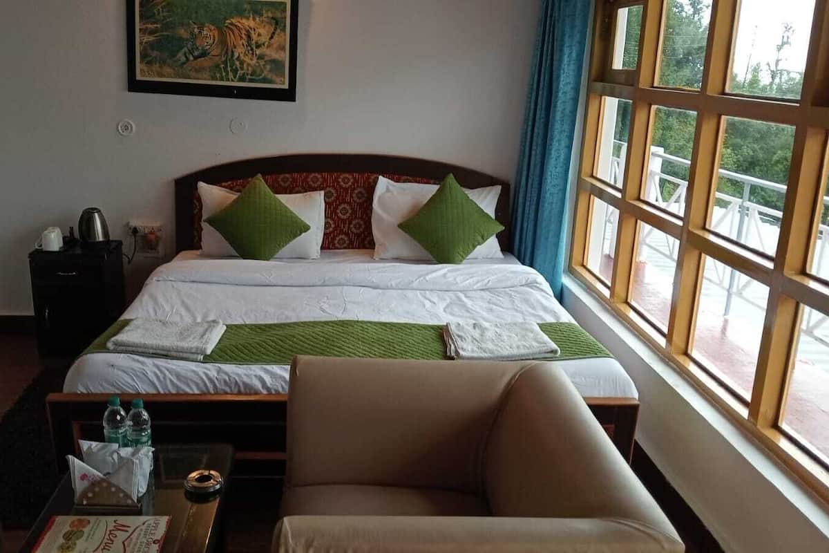 A hotel room with a bed, two armchairs, a small table with a bottle and a tissue box, and a window with a view of greenery.