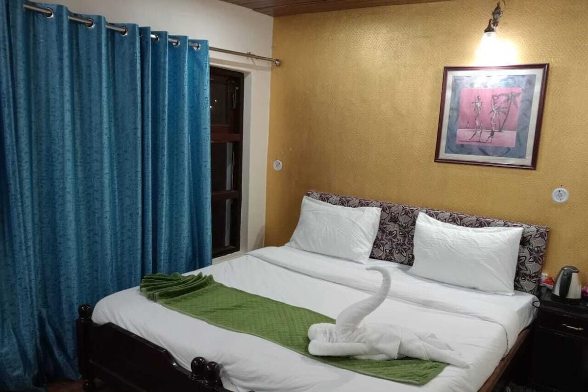A neatly made bed with white and green bedding, a framed picture on the wall, and a blue curtain.