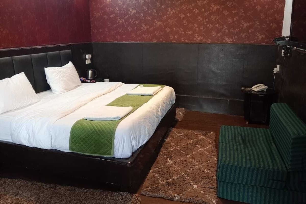 A bedroom with a bed, a green-striped chair, and a small table with a phone.