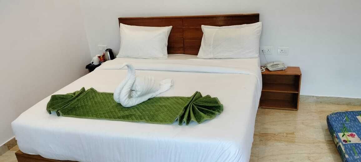 A neatly made bed with a green towel and a white swan decoration, a wooden nightstand with a phone, and a blue floral-patterned item on the floor.